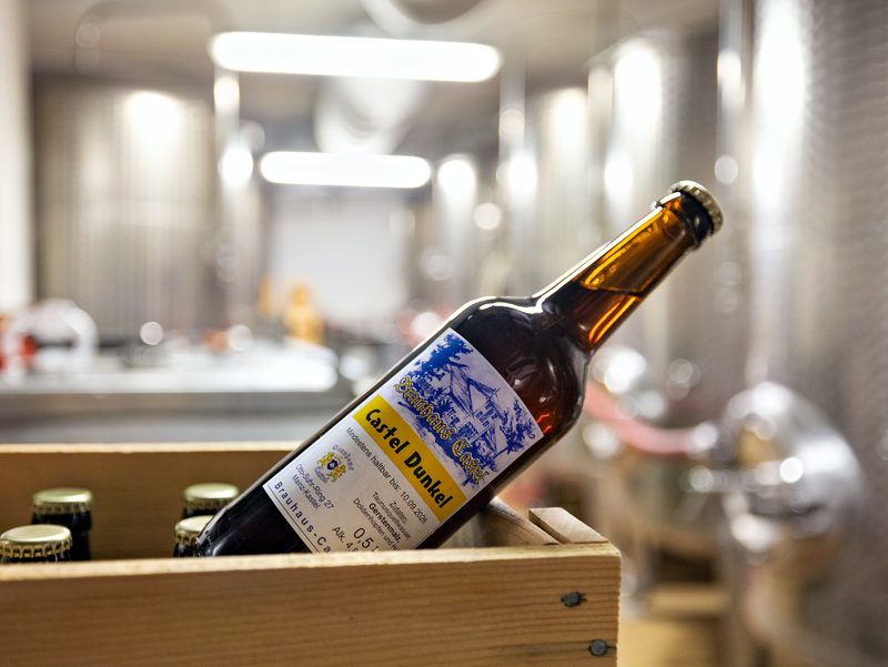 Flasche der Casteler Biermanufactur, liegend in einer Holzkiste im Lagerkeller